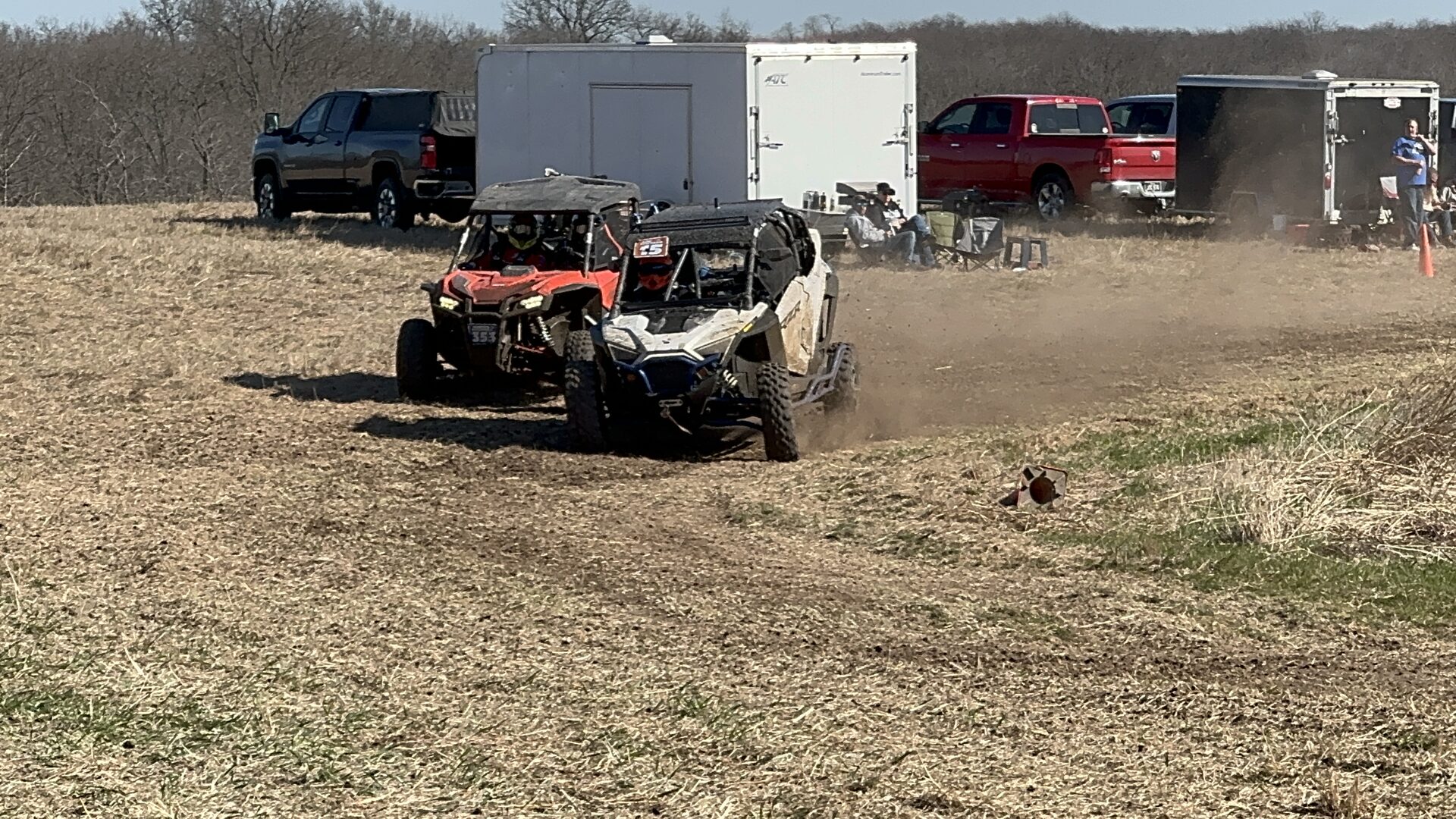 Two UTVs racing side by side across a dirt field