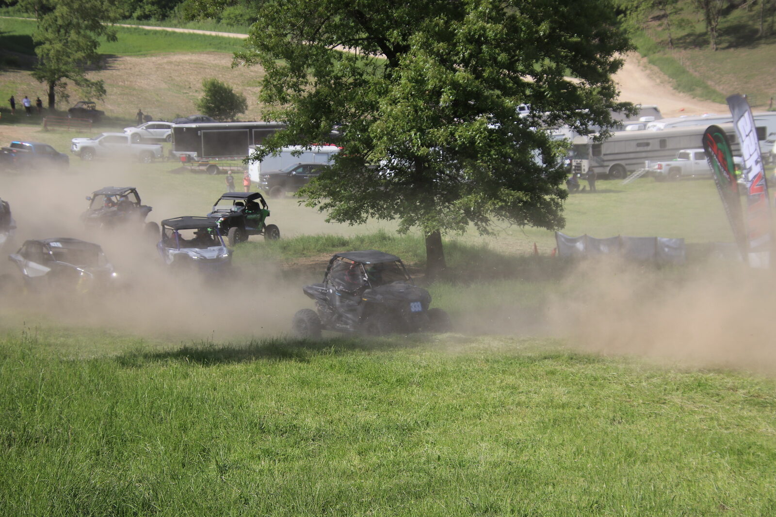 UTVs racing through trees, heavily obscured by dust